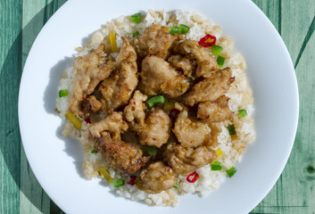 chicken in sweet and sour sauce and rice with vegetables on a white plate green background close-up