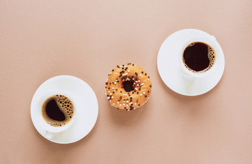 A tasty donut and two cups of hot coffee