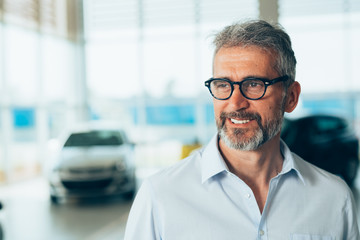 portrait of bearded sell agent in car dealers showroom