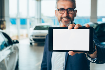 senior businessman holding tablet with blank screen in car showroom
