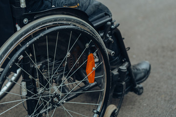 Fototapeta na wymiar Close-up of male hand on wheel of wheelchair during walk in park