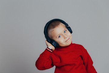 Portrait of an attractive smiling boy in a red sweater listening to music through headphones close-up