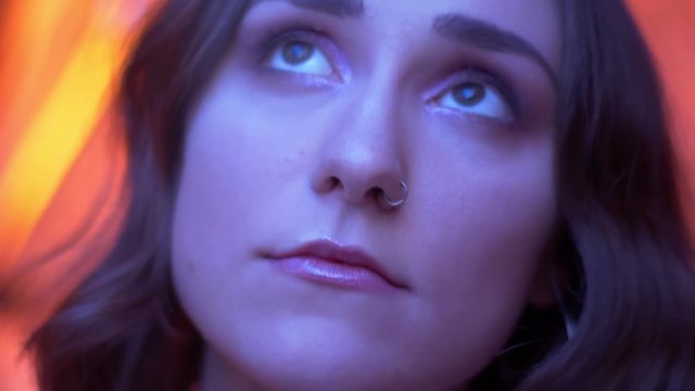 Closeup shoot of young attractive caucasian female face with nose piercing and beautiful eyes looking at camera with neon red background