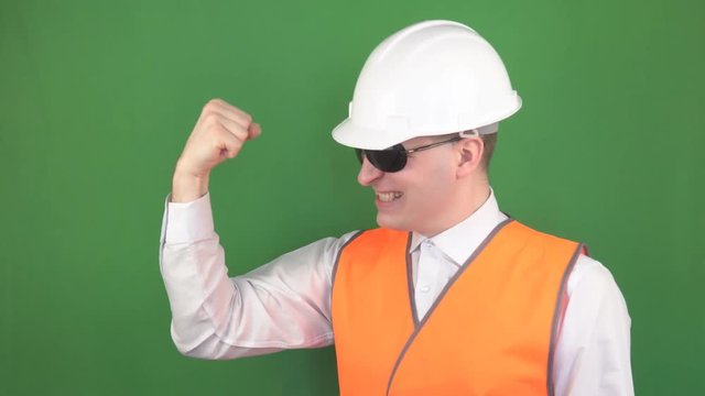 Young male chief in a signal vest and a protective helmet, black glasses, rejoices at the signed construction contract, background, chromakey, industry