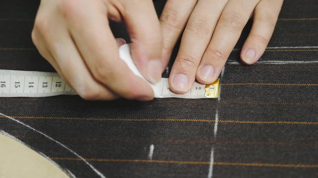 Woman hands making chalk markings on brown suit fabric