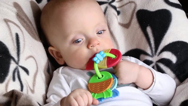 baby boy nibbles a teether toy. the child is sitting on the highchair. face close up