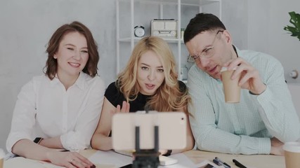 Creative stylish team of people go live online broadcasting from a smartphone. They are smiling and waving their hands. Broadcast on the Internet with a large number of subscribers and followers