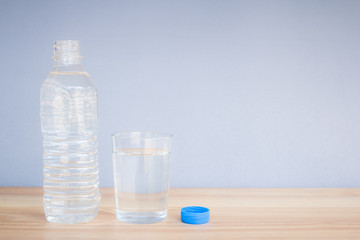 Refreshing natural mineral water in plastic bottle with transparent glass on wooden desk with copyspace