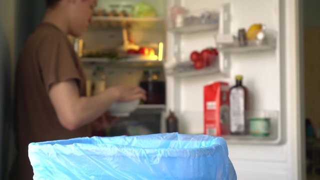 Young man throws spoiled vegetables out of the fridge. Household food waste in the wastebasket