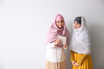 Young Muslim women with tablet computer on light background