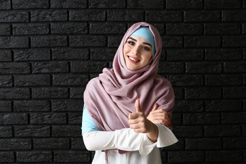 Beautiful Muslim woman showing thumb-up on dark background