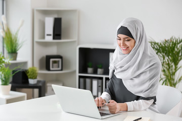 Muslim woman working on laptop in office