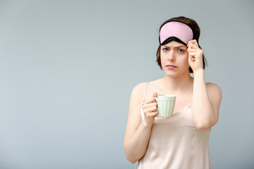 Sad woman with sleep mask and cup of coffee on color background