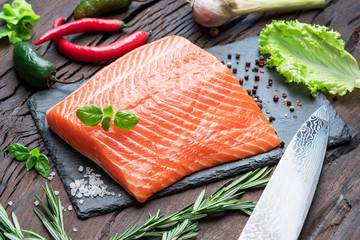 Fresh salmon fillet on black cutting board with herbs and spices.