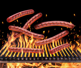 Sausages falling on the burning grill grate and tongues of fire flame.