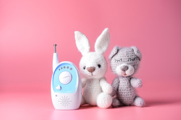 Modern baby monitor with toys on color background