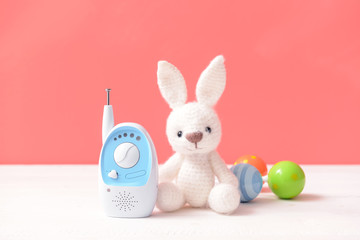 Modern baby monitor with toys on table against color background