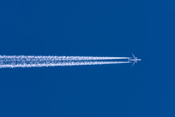 Airplanes leaving contrail trace from left to right on a clear blue sky.