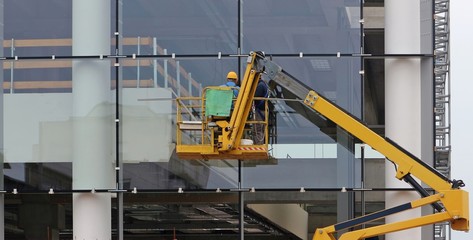 Workers on a cherry picker. They are finishing the glass facade of a building under renovation