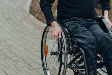 Close-up of male hand on wheel of wheelchair during walk in park