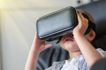 Child using new Virtual Reality, VR cardboard glasses. happy little boy with virtual reality headset sitting on sofa. Toned photo
