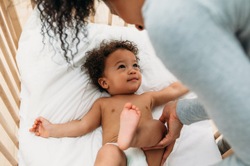 Woman touching leg of a newborn baby boy lying in a crib