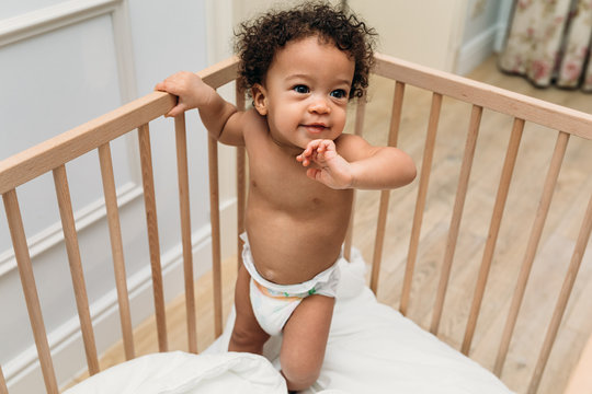 Curly Haired Toddler Wearing A Diaper In A Crib