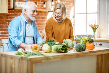 Cheerful senior couple making salad with healthy fresh ingredients on the kitchen at home. Concept of healthy eating in older age