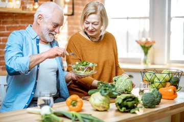Gardinen Cheerful senior couple eating salad standing together with healthy food on the kitchen at home. Concept of healthy nutrition in older age © rh2010