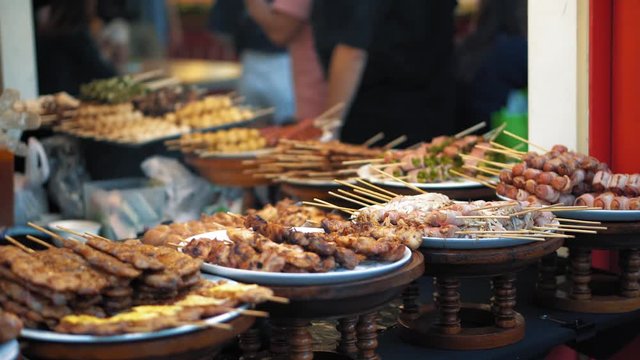 Traditional Asian food is sold at the night market in Thailand. Fried chicken pieces, sausages, bacon are appetizing on the plates