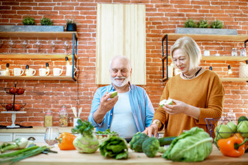 Cheerful senior couple eating fruits standing together with healthy food on the kitchen at home. Concept of healthy nutrition in older age