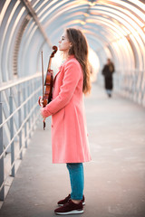 Obraz premium Young woman in glasses standing on the overhead passage holding a violin
