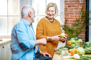 Cheerful senior couple eating fruits standing together with healthy food on the kitchen at home. Concept of healthy nutrition in older age