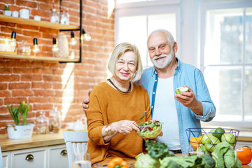 Portrait of a cheerful senior couple with salad and healthy food on the kitchen at home. Concept of...