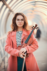 Young woman in pink coat standing on the upper pedestrian crossing holding a violin