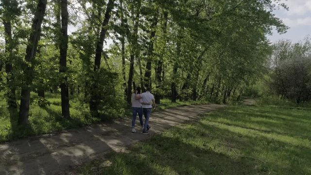 Lovers (man and woman) dressed in blue jeans and white t-shirts , holding hands, hugging, walking on a sandy road, shooting from the back, summer/spring Sunny day