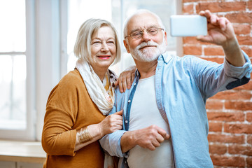 Happy senior couple making selfie photo or talking online using smart phone at home