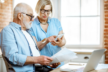 Senior couple with embarrassed emotions calculating some bills or taxes sitting with laptop on the...