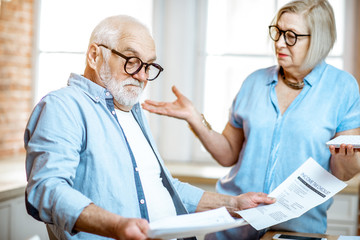 Senior couple with shocked emotions looking on high bills or taxes sitting with laptop on the...