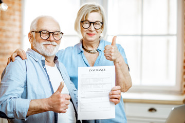 Portrait of a happy senior couple holding insurance agreement indoors