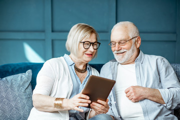 Lovely senior couple dressed casually using digital tablet while sitting together on the comfortable couch at home