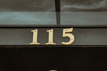 Building Number 115 in gold serif font on a black building background. One Hundred Fifteen