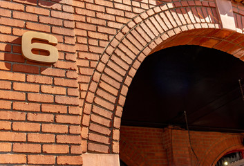Building Number 6 in bronze sans serif font on a red brick building background. Number 6. with a long hard shadow.