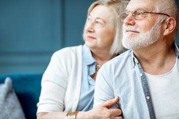 Portrait of a beautiful senior couple embracing each other, sitting on the couch at home - obrazy, fototapety, plakaty