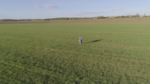 A man in a blue shirt and jeans holding the hand of a girl in a blue dress, they go on the field, aerial photography on a Sunny summer day, the camera moves away from a couple of lovers
