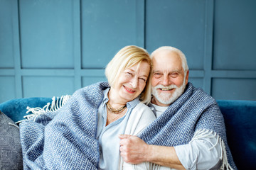 Portrait of a lovely senior couple feeling cozy and warm, sitting wrapped with plaid on the couch at home