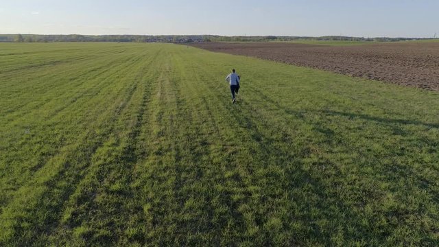A man/guy dressed in jeans and a shirt with a jacket in his hand runs across the open field to meet a girl in a blue dress on a Sunny spring/summer day, aerial photography, 