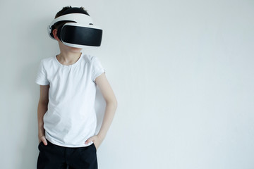 Young boy wearing virtual  reality headset and glasses, white t-shirt and black pants on white wall, playing with reality. The concept of modern recreation. Futuristic- digital technology concept