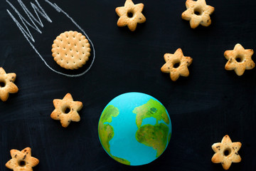 top view  handmade model  of Earth planet, cookie meteorite   and cookies in the shape of stars on the chalkboard , space and astronomy concept