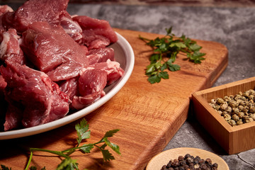 pieces of red veal meat on a wooden board and next to different spices